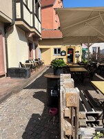 Un área de café al aire libre con mesas y sillas, un contenedor de basura y una planta en maceta.