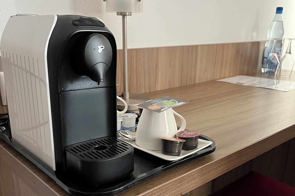 A coffee maker, a cup of coffee, a water bottle, and a small pitcher on a wooden table.