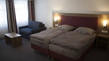 Habitació d'hotel amb llit doble, una cadira, una tauleta de nit i una meseta de cabdal.