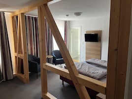 Una habitación con una cama, una silla, un televisor montado en la pared y una puerta.