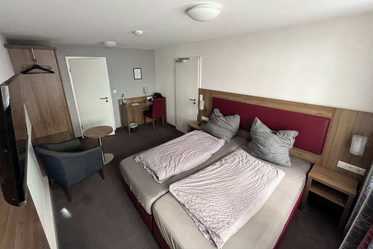 A hotel room with a bed, a desk, a chair, a small table, and a wardrobe.