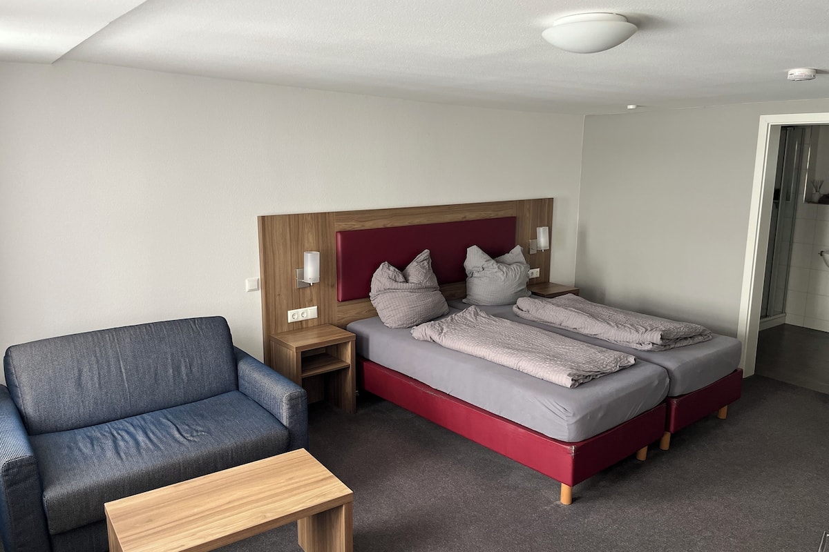 A hotel room with a bed, a chair, a nightstand, and a table.
