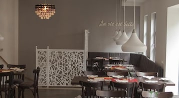 Un área de comedor moderna con varias mesas y sillas, un separador blanco decorativo y lámparas colgantes.
