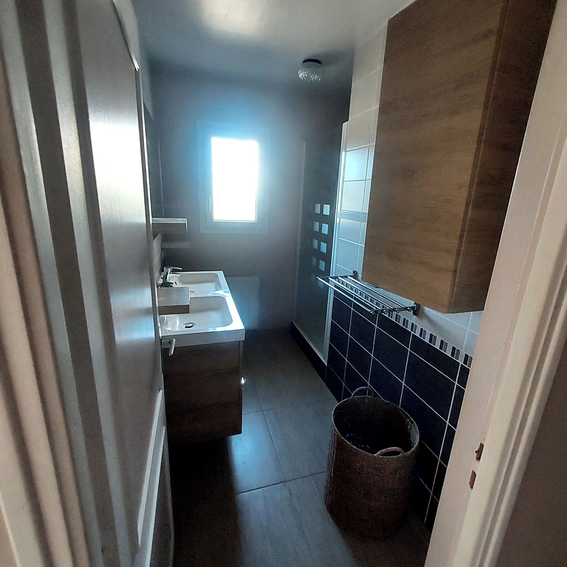 Een smalle badkamer met een wastafel, spiegel en een raam voor natuurlijk licht.