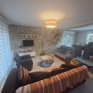 A living room with a sofa, armchairs, a coffee table, a TV, and a stone wall. - Small Breton house from Saturday to Saturday (Ploubazlanec)