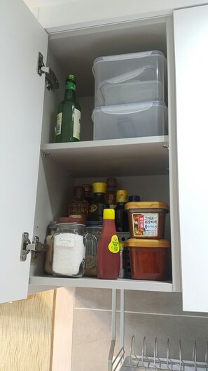 A kitchen cabinet with storage containers, a bottle of ketchup, and jars of condiments. - Jeju 5th Apartment in Baekgang Supia (Jeju City)