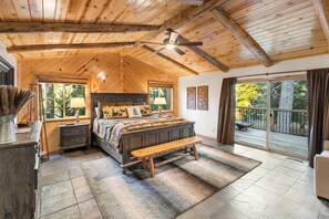 Un dormitorio espacioso con una cama grande, techo de madera y vistas al exterior a través de una puerta corrediza de vidrio.