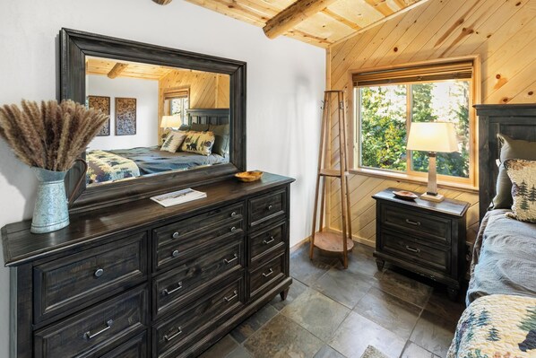 A bedroom with a large mirror, dark wooden dresser, and a bed with a quilt.