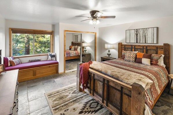 Un dormitorio con una cama grande, un asiento junto a la ventana, un ventilador de techo y vistas al exterior.