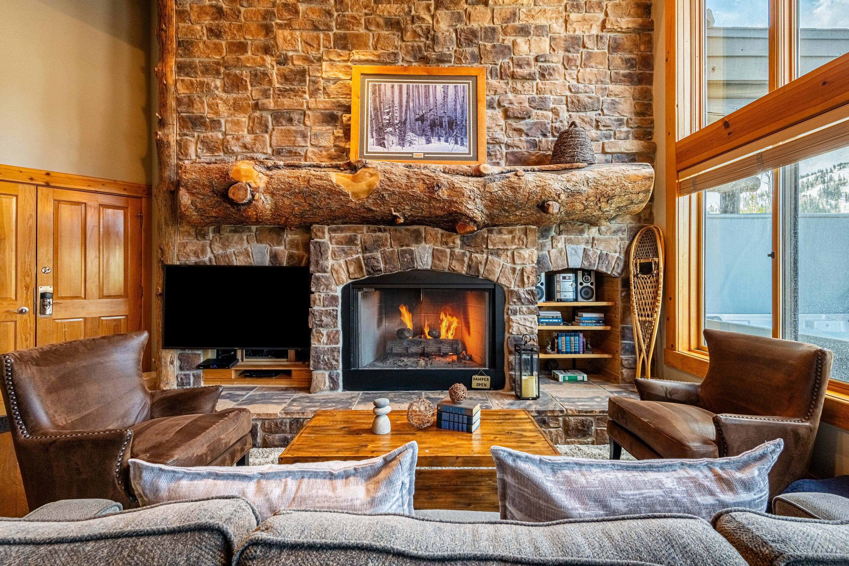A stone fireplace with a TV, leather chairs, a coffee table, and a bookshelf.