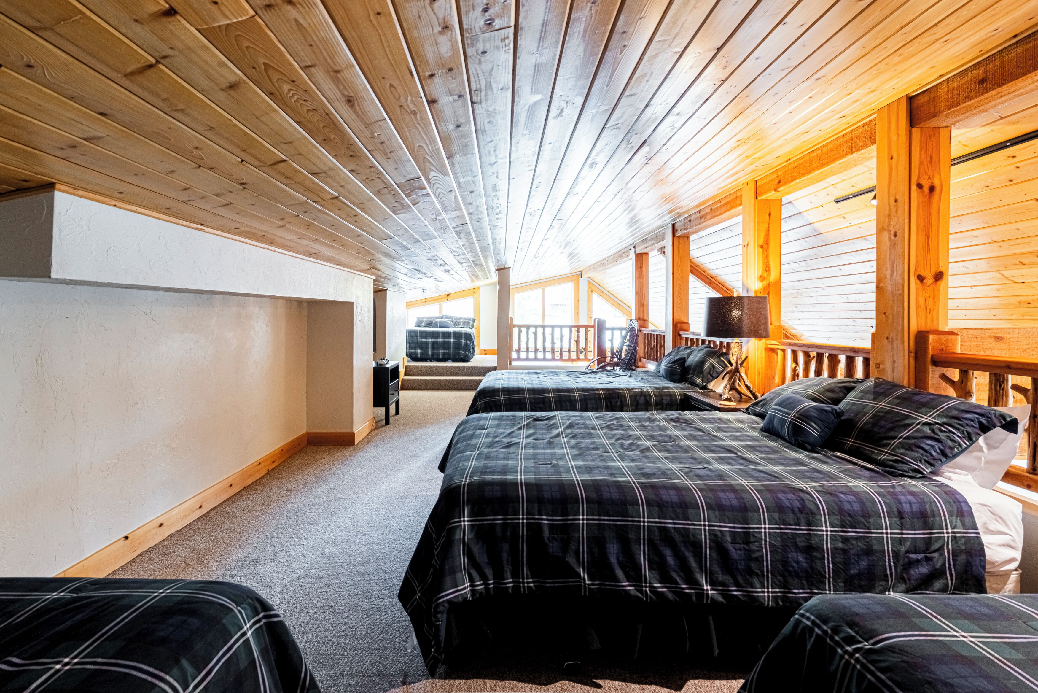 A cabin interior with two beds, wooden ceiling beams, and a view of the outdoors.