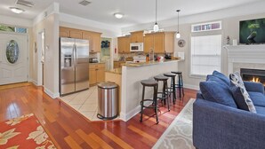 A modern kitchen with stainless steel appliances, a central island with bar stools, and a cozy living area with a fireplace. - Lions Bridge: Modern 3 bedroom Home in Historic Lincolnville - walk to Historic (St. Augustine)