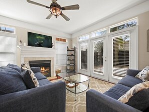Una sala de estar con chimenea, ventilador de techo y un ventanal con persianas.