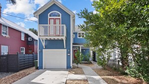 A two-story house with a blue exterior, a white garage door, and a balcony with red railings. - Lions Bridge: Modern 3 bedroom Home in Historic Lincolnville - walk to Historic (St. Augustine)
