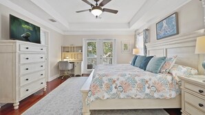 A bedroom with a bed, a desk, a chair, a dresser, a ceiling fan, and a television. - Lions Bridge: Modern 3 bedroom Home in Historic Lincolnville - walk to Historic (St. Augustine)
