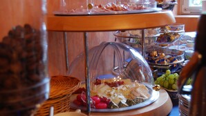 A buffet with various food items and a glass dome covering a selection of cheeses and fruits. - Hotel Wagner (Bad Wimpfen)