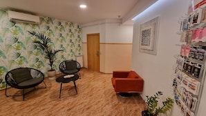 Ein Zimmer mit Holzboden, zwei schwarzen Stühlen, einem roten Sofa, einer Topfpflanze und einer Wand mit floralem Wandpapier.