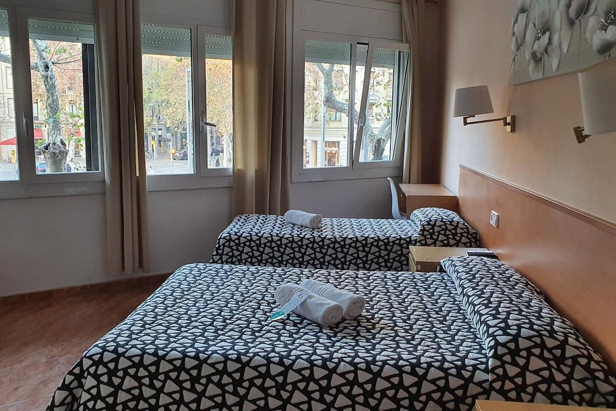 A hotel room with two beds, a wooden bench, a desk, and a chair.