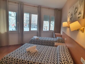 Une chambre d’hôtel avec deux lits, de grandes fenêtres et un tableau au mur.