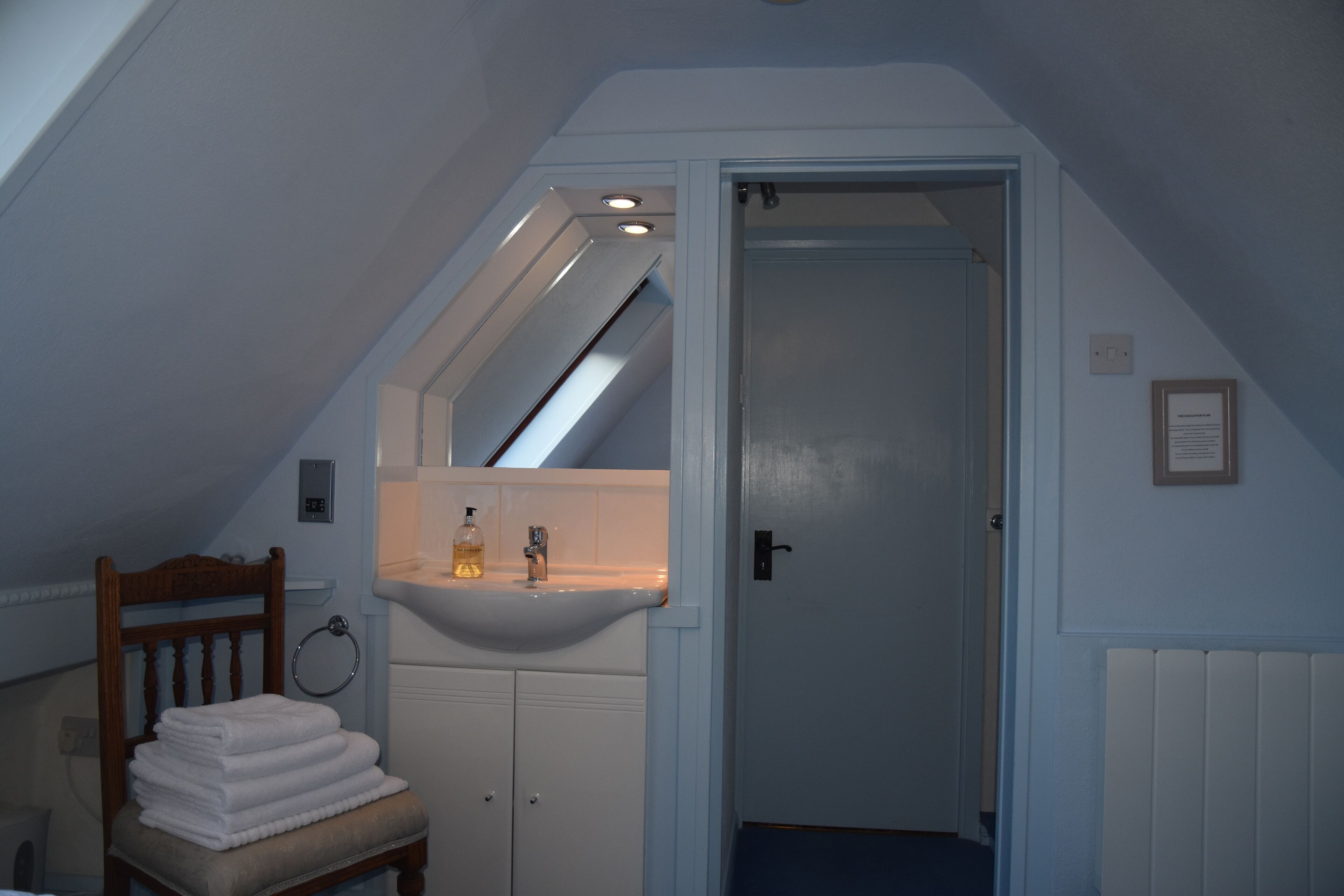 A bathroom with a white sink, a wooden chair with towels, and a door leading to another room.