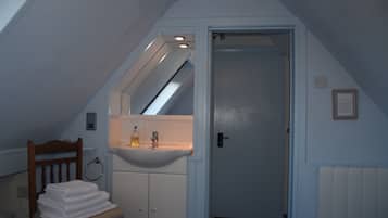 A bathroom with a white sink, a wooden chair with towels, and a door leading to another room.