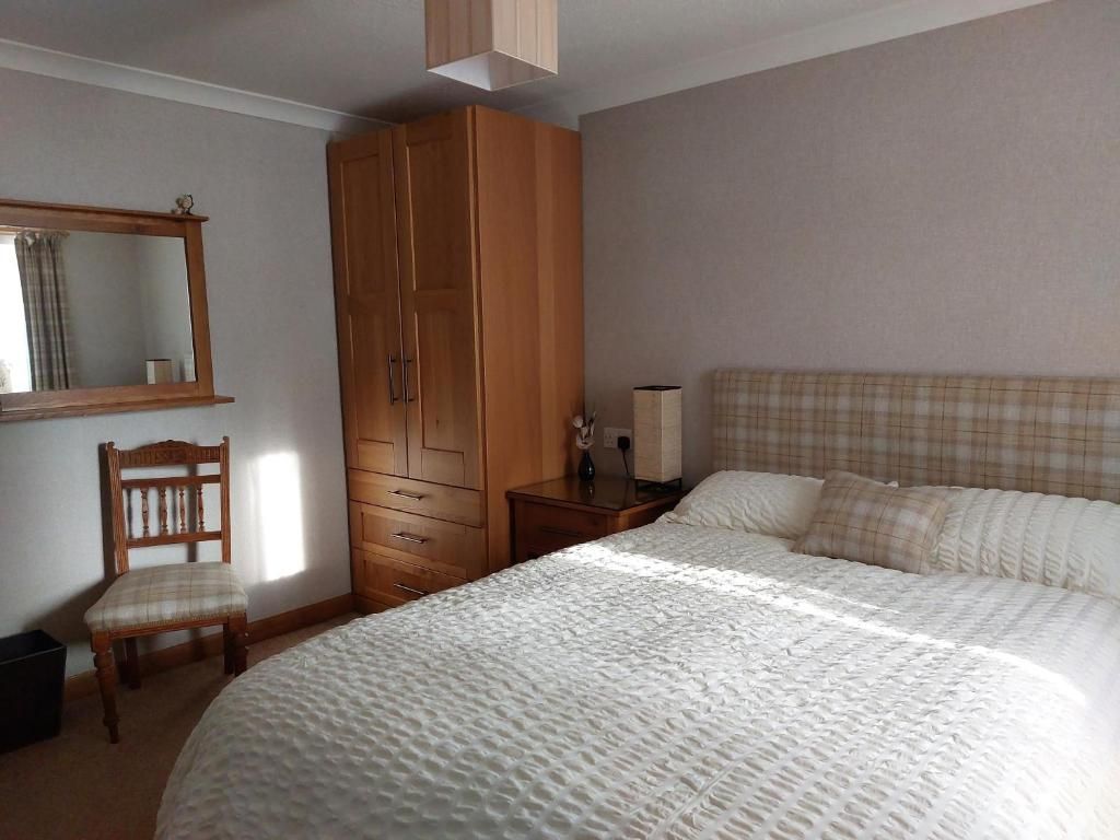 Ein Schlafzimmer mit einem großen Bett, einem Holzschrank, einem Sessel, einem Nachttisch und einem Spiegel.