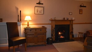 Una sala de estar acogedora con chimenea, un aparador de madera, una silla y una lámpara.