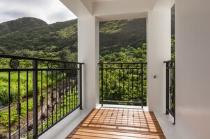 Un balcón con piso de madera y baranda de metal negro, con vistas a un paisaje verde y exuberante con colinas al fondo.