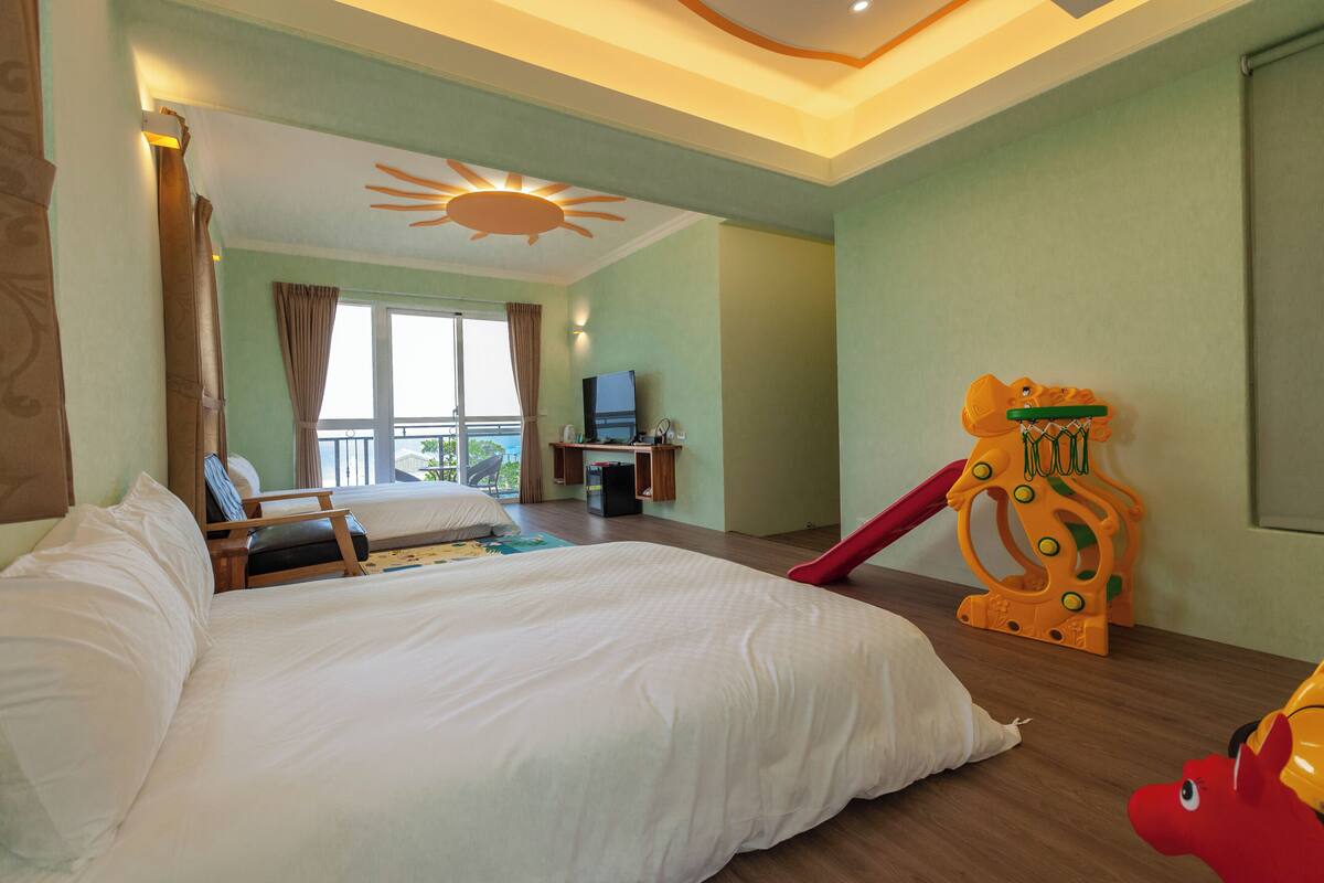 A hotel room with a bed, a desk, a television, and a children's play area.