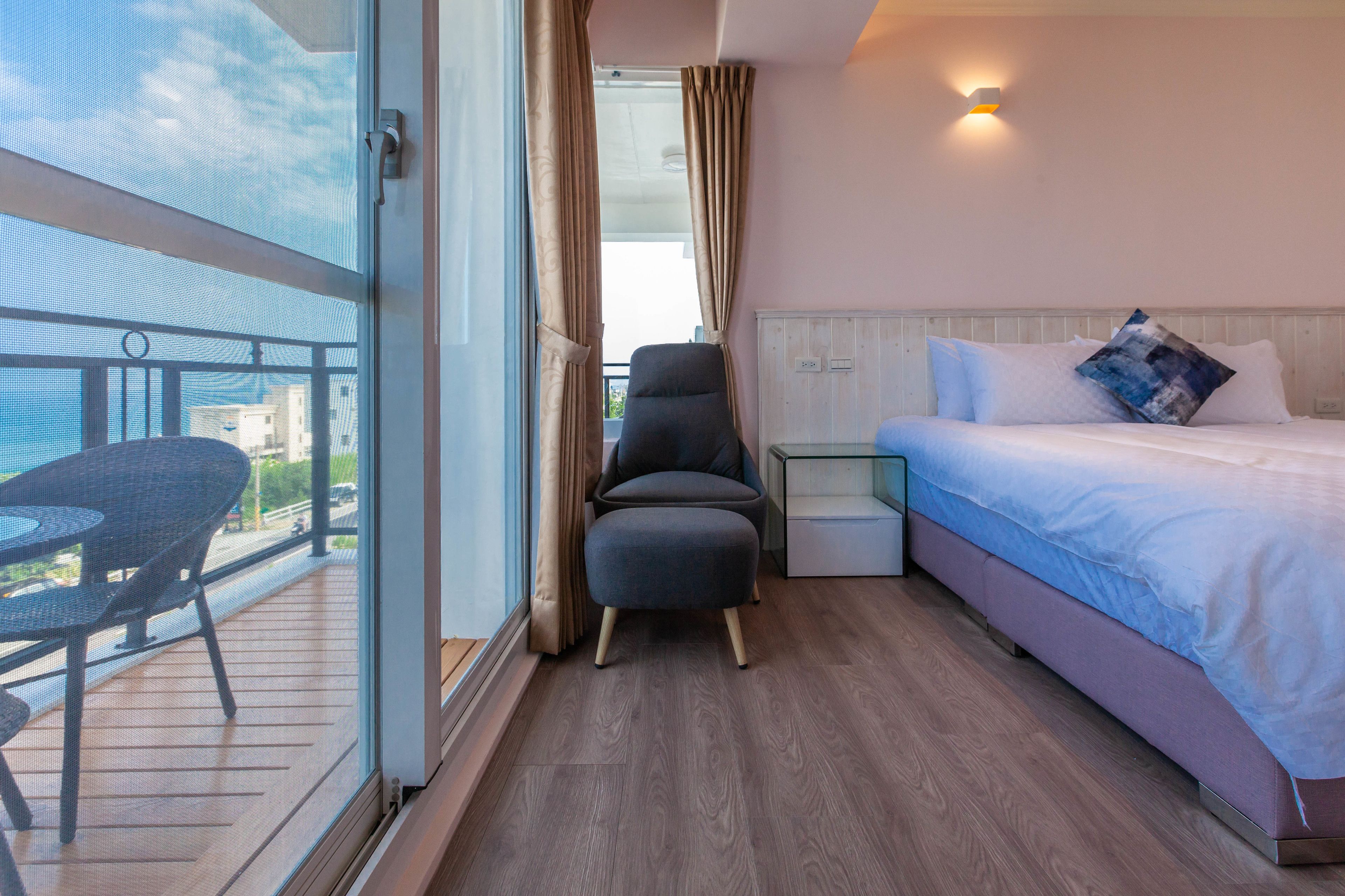 Habitación de hotel con cama, una silla, una mesita y un balcón con mesa y sillas.