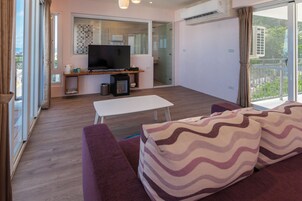Una sala de estar moderna con un televisor de pantalla plana, un sofá con cojines estampados, una mesa de centro y un balcón con vistas.
