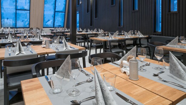 Un restaurant dont les tables sont dressées pour le service, avec un intérieur moderne agrémenté de panneaux en bois et de grandes fenêtres.