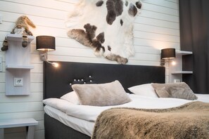 A bedroom with a bed, two wall-mounted lamps, a mounted cowhide, and a stuffed toy. - Santa's Igloos Arctic Circle (Rovaniemi)