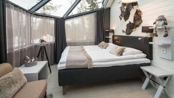 Un dormitorio moderno con tragaluces, una cama con ropa blanca, un adorno de cabeza de piel montado, y una pequeña estantería con objetos decorativos.
