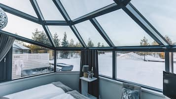 Une chambre moderne dotée d’un plafond en verre, d’un lit, d’une chaise et offrant une vue sur un paysage enneigé.