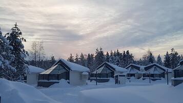 A row of snow-covered cabins with a clear sky and trees in the background.