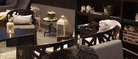 A cozy room with a sofa, a chair, a small table, and a shelf with various items.
