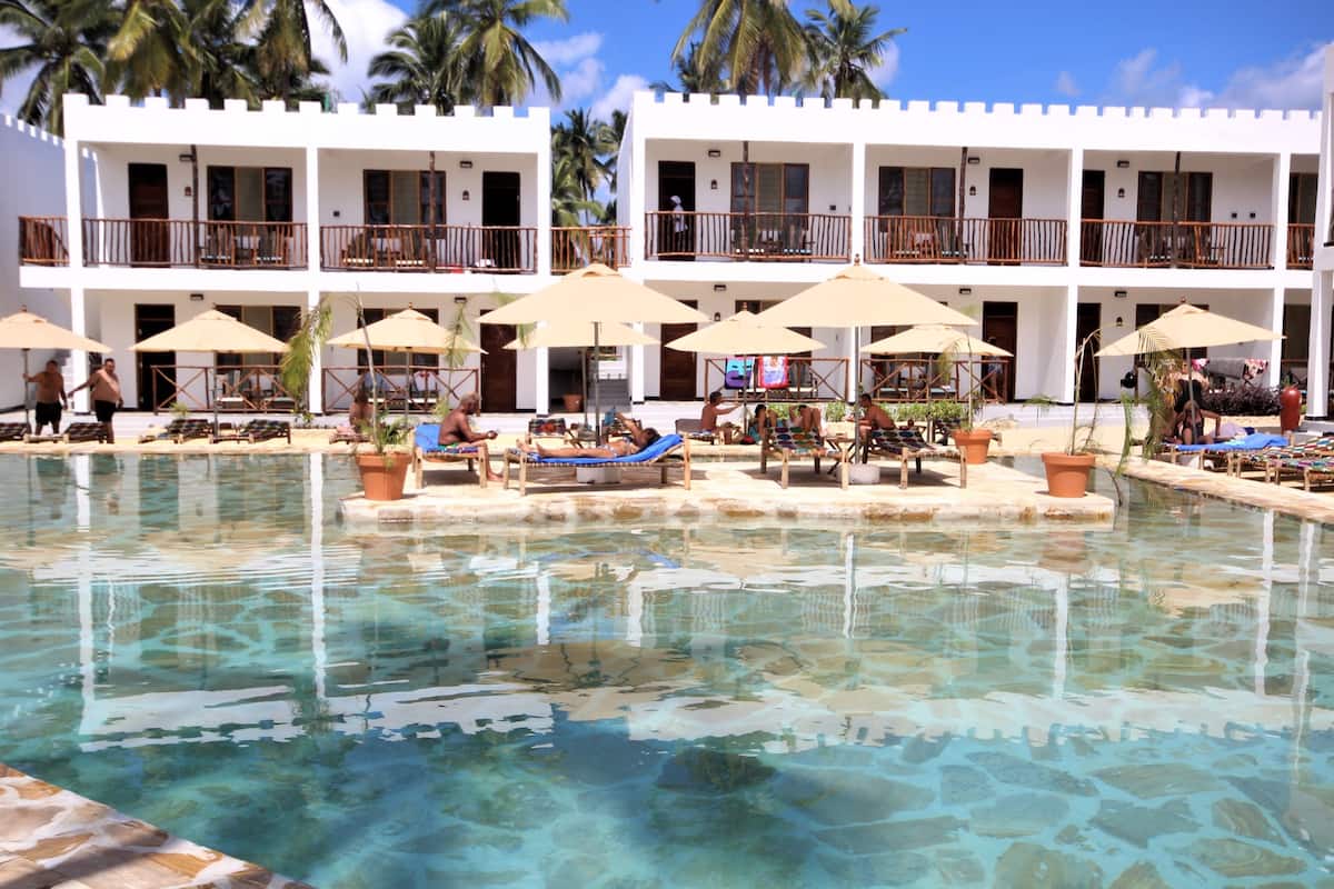 A pool area with clear water, lounge chairs, umbrellas, and a building with balconies.