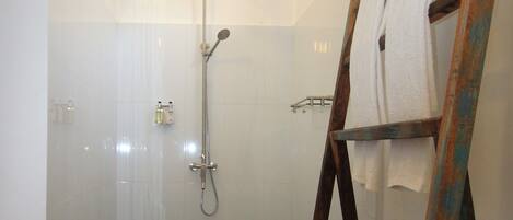 A bathroom with a shower, a wooden bench with towels, and a framed picture on the wall.