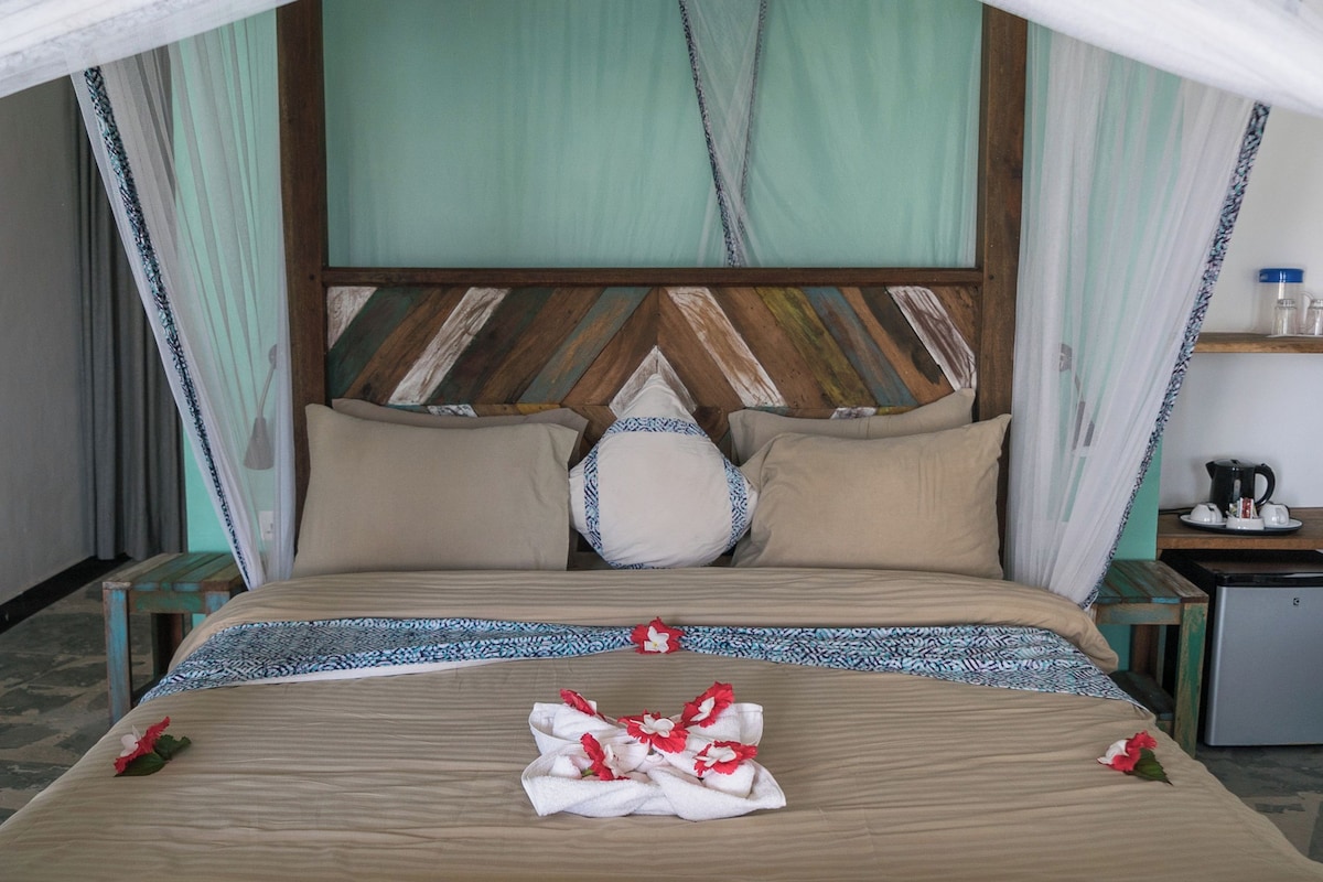 A bed with a wooden headboard, a bedside table, and a small desk with a kettle.