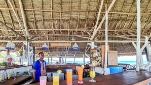 A beachside bar with a thatched roof, wooden bar counter, and various drinks. - Zanzibar Bay Resort (Marumbi)