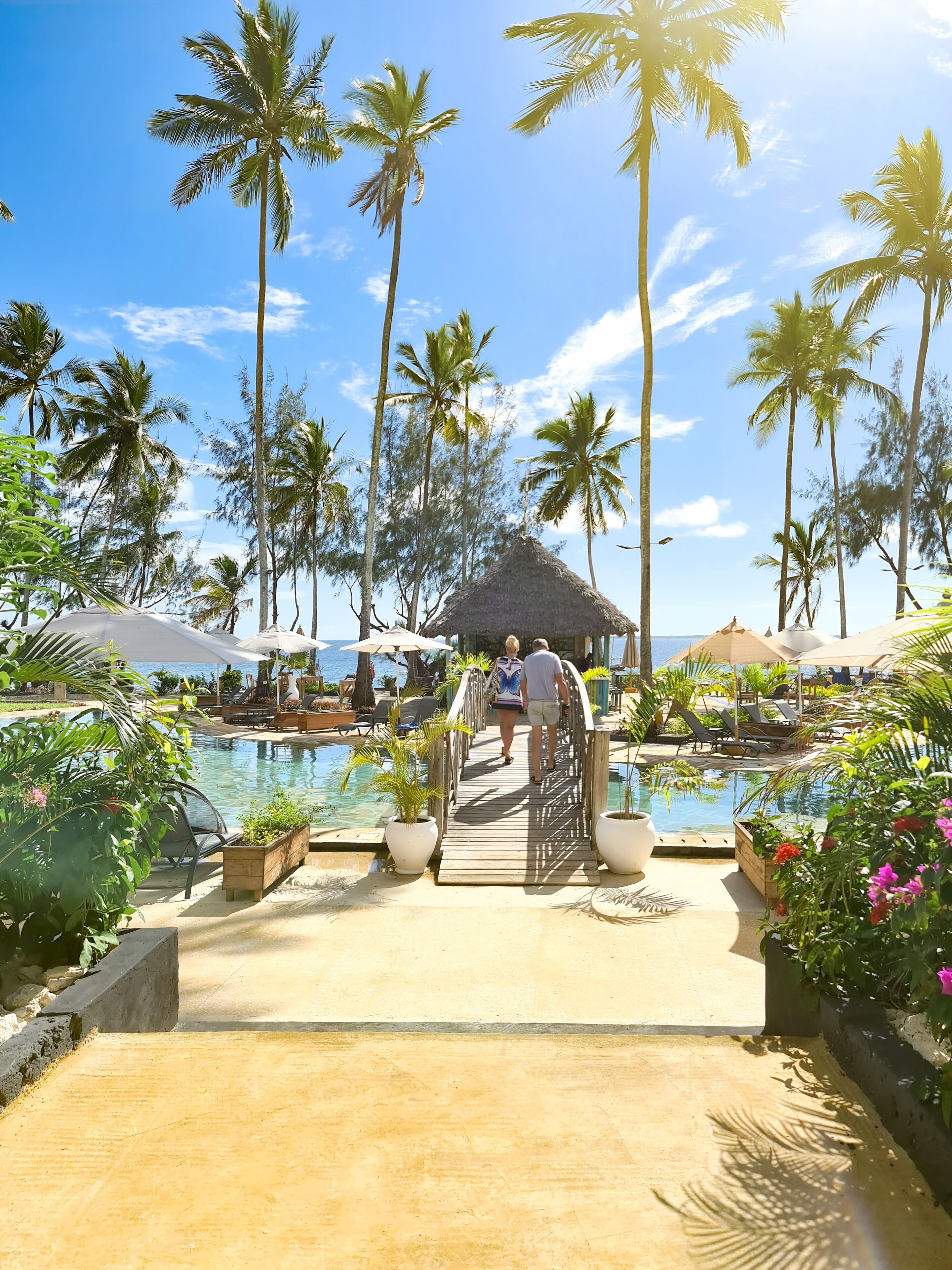 A resort pool area with a wooden deck, palm trees, and lounge chairs.