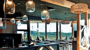 Un restaurante moderno con una barra central, lámparas colgantes y amplias ventanas que ofrecen vistas al exterior.