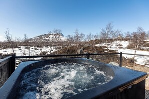 A hot tub with a view of a snowy landscape and a mountain in the background.