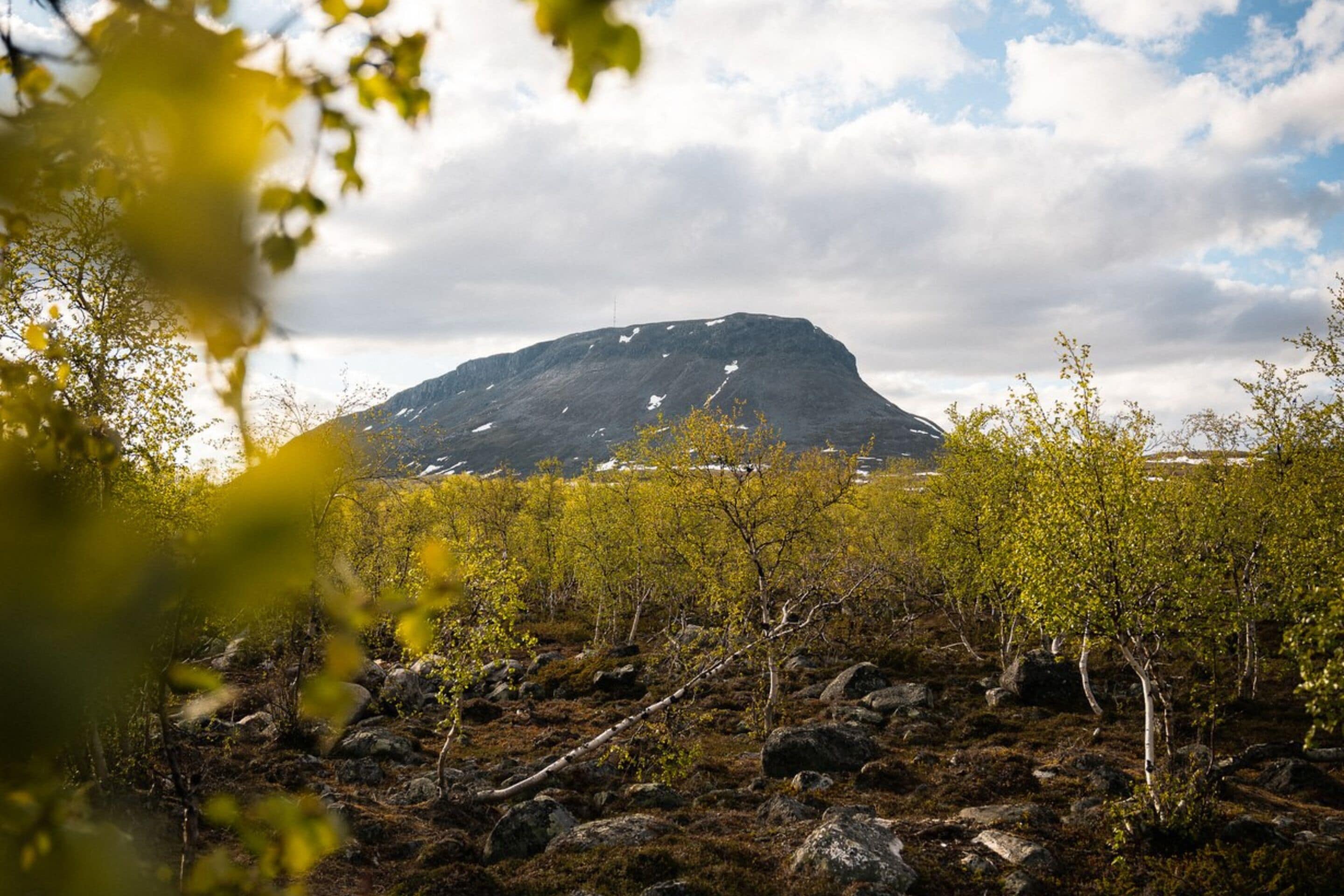 Ein Berg mit Schneeflecken, umgeben von felsigem Gelände und spärlicher Vegetation.