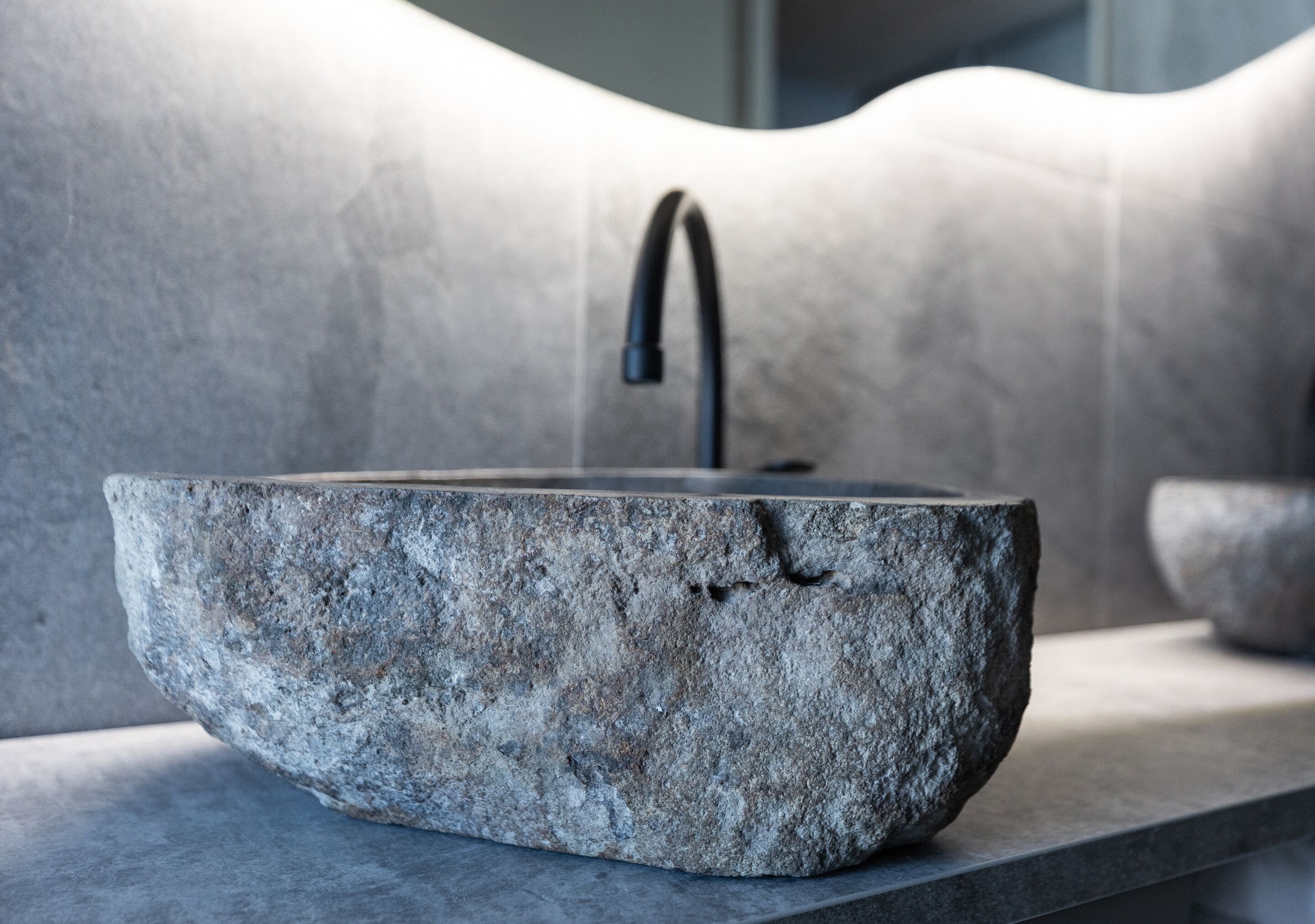 A stone basin with a faucet, set against a textured wall.