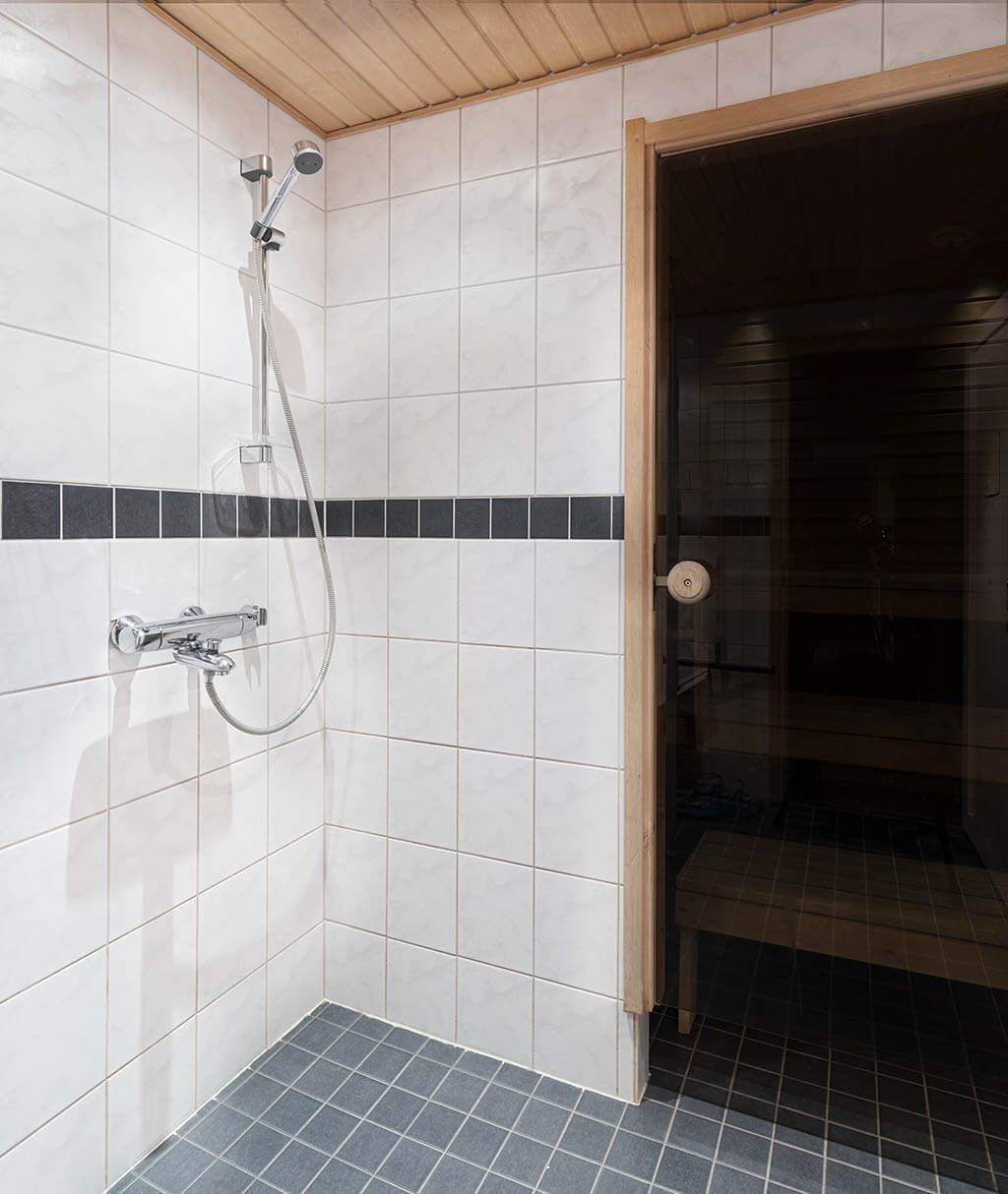 A bathroom with white tiled walls, a black and white striped tile border, a shower with a handheld showerhead, and a glass shower enclosure.