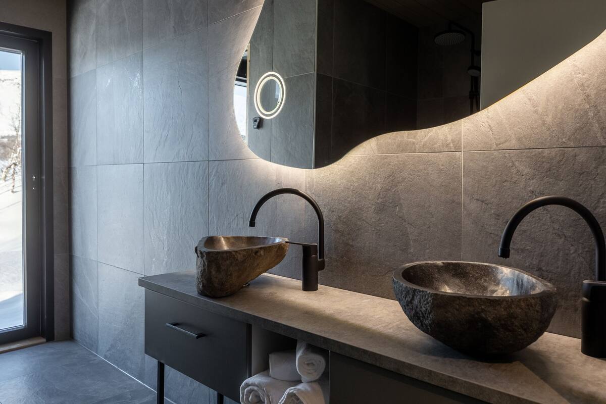Une salle de bain moderne avec un grand miroir, deux vasques en pierre et un porte-serviettes.