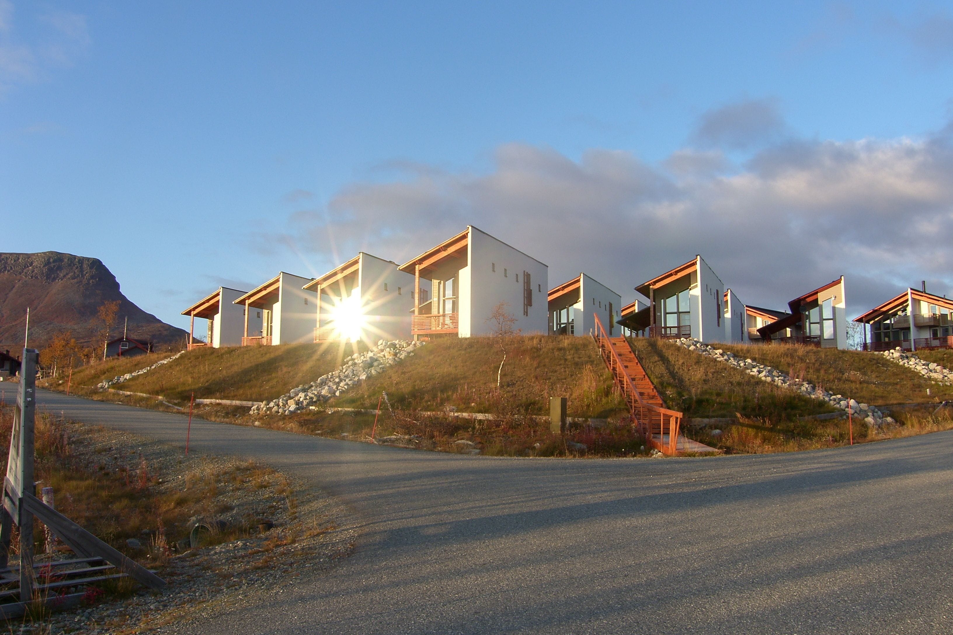A modern residential building with multiple units, a sloped roof, and a staircase leading to the entrance.
