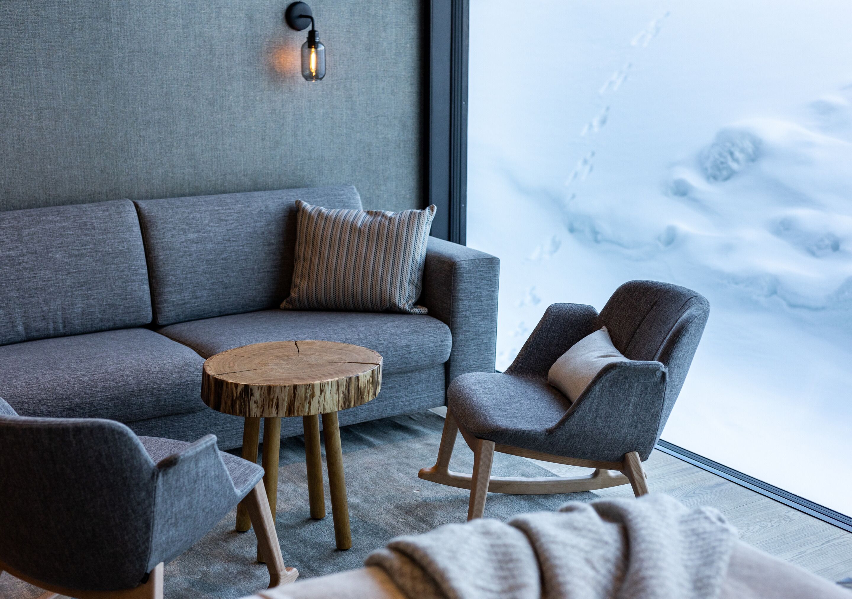 Una sala moderna con un sofá gris, una mesa de centro de madera y un sillón mecedora.
